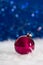 Burgundy Christmas ball on white fur with garland lights on blue