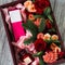 A burgundy wooden box with red roses, branches of a green Christmas tree, a pink perfume box in a glass jar lies on a wooden gray