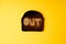 Burn out concept. one slice of dark burnt charred white bread with word Out on it on yellow background