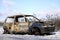 Burned, destroyed car standing on the side of the road in the winter.