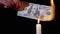 Burning 100 Dollar Bill over a Smoky Candle Flame on a Black Background.