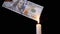 Burning 100 Dollar Bill over a Smoky Candle Flame on a Black Background.