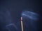 Burning aromatic incense stick with ash and smoke on blue background with copy space.