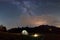 Burning bonfire near the tent against backdrop of powerful mountains under starry sky on which Milky Way is visible