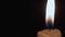 A burning candle close-up in a dark room, the flame from the candle illuminates the space around. Yellow-white fire from