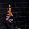 Burning candle in female hands in black gloves. Brick wall background. Square frame. Close-up. Theme holiday halloween