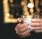 A burning candle in the hands of a girl on the background of new year garlands with a blurred focus in the form of a Golden bokeh