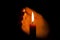 A burning candle at night, protected by the hand of a woman. Candle flame glowing on a dark background with free space for text.