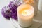 Burning candle and violet allium flowers on white tray