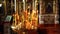 Burning candles stand in golden church chandelier. There are many holy icons on a background.