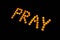 Burning candles. Word Pray made with burning yellow candles on black background.
