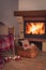 Burning fireplace and rattan armchair with red wool plaid, cozy sleepers with pompons and basket with knitting stuff