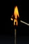 Burning match on a black background. A match sets fire to another match against a dark background.