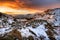 Burning orange clouds in sky at sunrise with snow covered mountains and old stone wall. Lake District, UK.