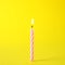 Burning pink striped birthday candle on yellow