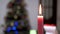 Burning Red Candle with a Bright Flame on a Blurred Christmas Tree Background