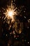 Burning sparkler stands in a glass. Dark background with defocused multi-colored lights of garland.