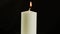 A burning white candle on a black background or in the dark. Concept: Symbol of Sorrow and World Cancer Day