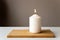 Burning white candle on wooden stand on white wall on beige background