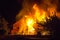 Burning wooden house at night. Bright orange flames and dense sm