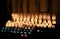 Burning yellow candles on a stand inside a church.  Burning candles in sconces on black blue background