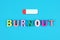 Burnout word from multicolored wooden letters and low battery icon on bright blue background