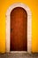 Burnt orange arch shaped door against a yellow wall
