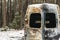 A burnt-out minivan stands near the forest in winter