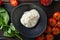 Burrata Handmade cheese Black plate served with fresh raw tomatoes and basil leaves , flatlay on a dark woodold background,
