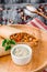 Burrito with vegetables, decorated with soy sprouts, served with cream sauce, on wooden plate on gray wooden background