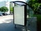 Bus shelter of glass & aluminum structure in park-like setting with empty poster ad area