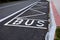 Bus stop consisting of a reserved place with the word bus. Horizontal traffic sign white lines. The concrete curb is rounded due t