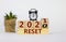 Business and 2021 new year reset symbol. Fliped wooden cube and changed words `reset 2020` to `reset 2021`. Alarm clock, plant