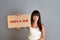 Business and advertising. A young brunette with a piercing, holding in one hand a cardboard with text NEED A JOB. Gray background