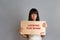 Business and advertising. A young brunette woman with a piercing, holding a cardboard with text LOOKING FOR WORK. Gray background