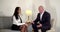 A business bald middle-aged man in a suit sits in a bright room on a chair, opposite him sits a business woman in