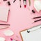 Business composition with clipboard, tulips, cosmetics and accessory on pink background. Top view. Flat lay. Home feminine desk.