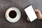 Business concept. Black coffee or hot espresso in a white ceramic cup and hand hold white screen on a smartphone or mobile on a