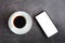 Business concept. Black coffee or hot espresso in a white ceramic cup and white screen on a smartphone or mobile on a dark table