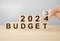 Business concept of planning 2024. Businessman flips wooden cube and changes words BUDGET 2023 to BUDGET 2024. Phrase