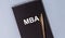 Business educatuion concept. inscription text MBA acronym on black spiral notebook with golden pen on blue table, flatlay, master