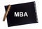 Business educatuion. inscription text MBA acronym on black sheet torn from spiral notebook with golden pen on white table, flatlay