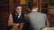 Business employees chatting in library. Professor reading book in classical library cabinet. Men in suit chat talking or