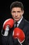 Business fighter. Portrait of confident businessman in red boxing gloves standing against black background