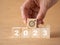 Business growth target. Businessman hand holding wooden cubes with number 2023, graph and target icon on brown paper background.