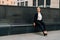 A business lady in a black, stern suit sits on a bench outside work at lunchtime. Customer`s waiting concept