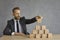 Business leader sitting at office table and building pyramid out of wooden cubes