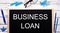 BUSINESS LOAN written on a black note-board next to blue paper clips, pencils and a pen