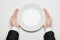 Business lunch and healthy food theme: man\'s hand in a black suit holding a white empty plate and shows finger gesture on an