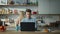 Business man conducting video conference with laptop on kitchen. Wife cooking.